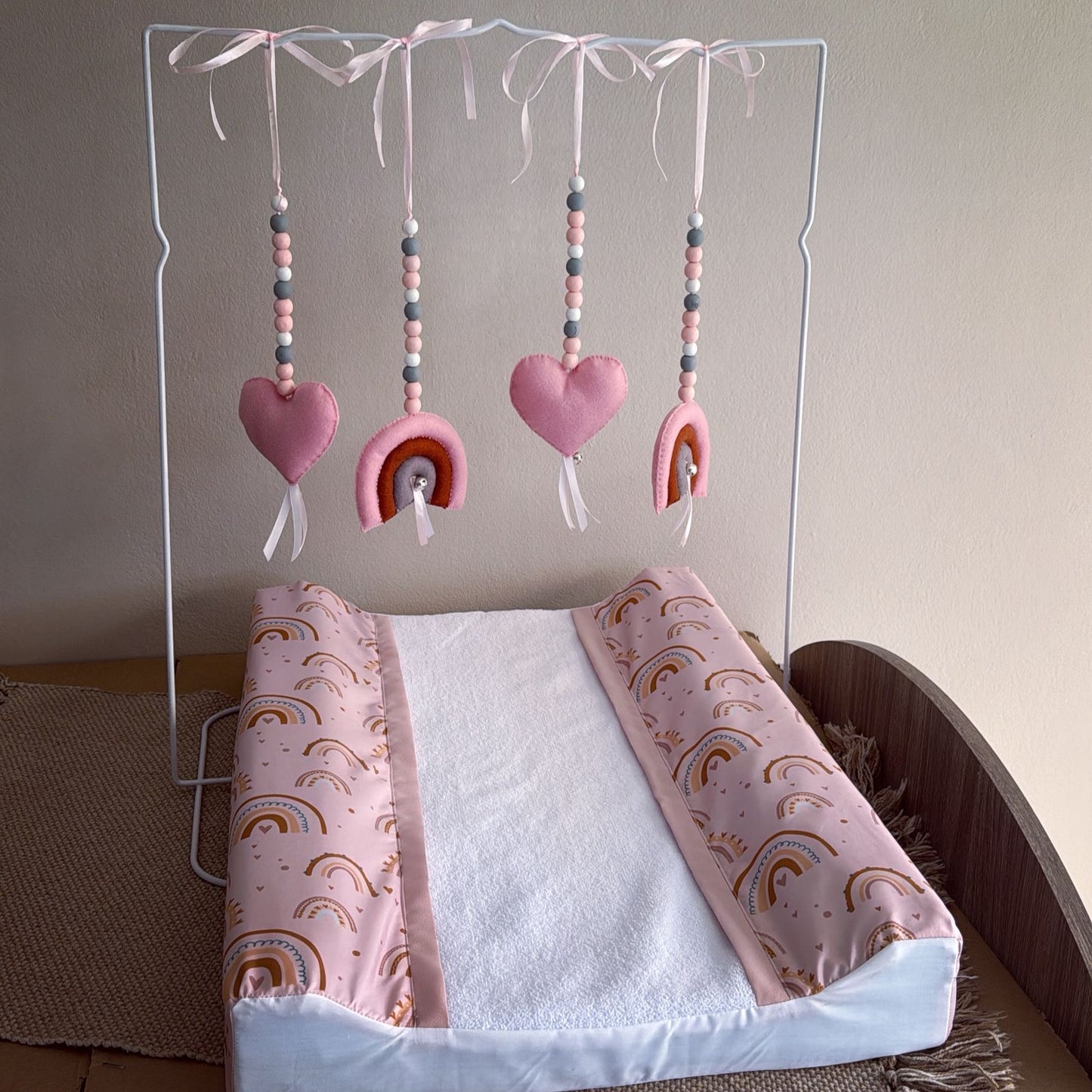 Baby crib with pink and rainbow-patterned bedding and mobile above.