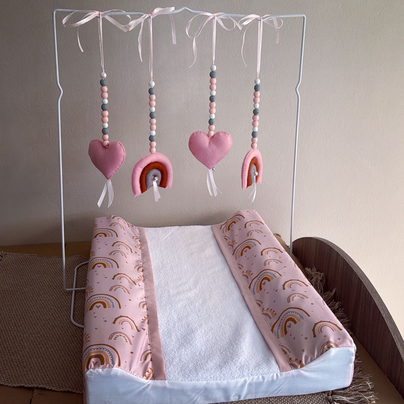 Baby crib with pink and rainbow-patterned bedding and mobile above.