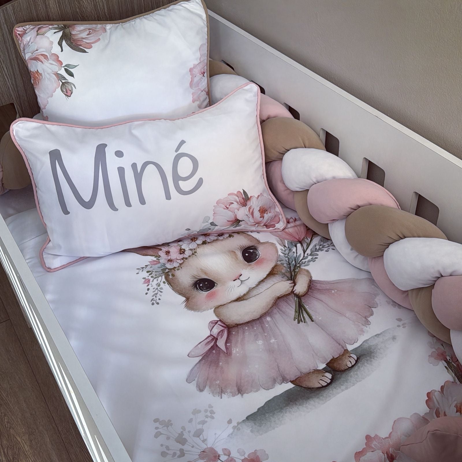 Children's bedding set with a bunny design and 'Miné' pillow in a crib.