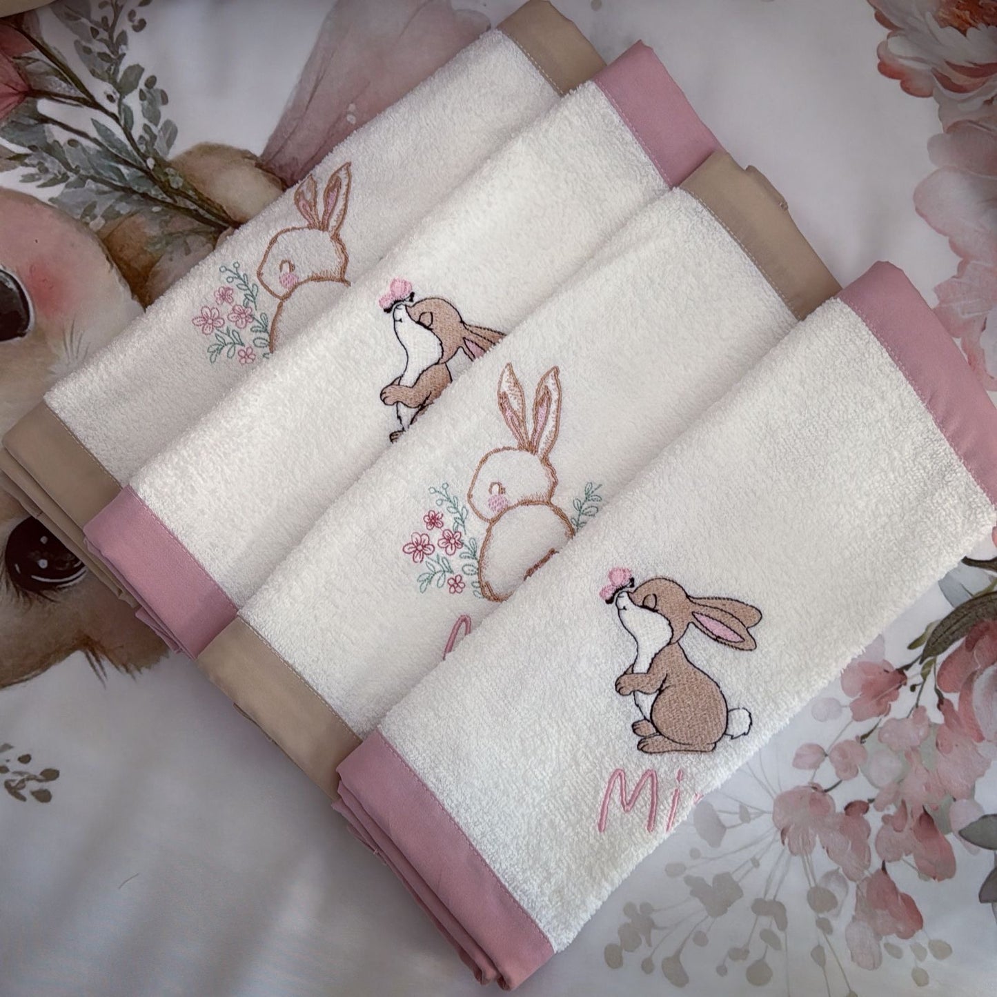 Set of folded towels with embroidered bunny designs on a floral background