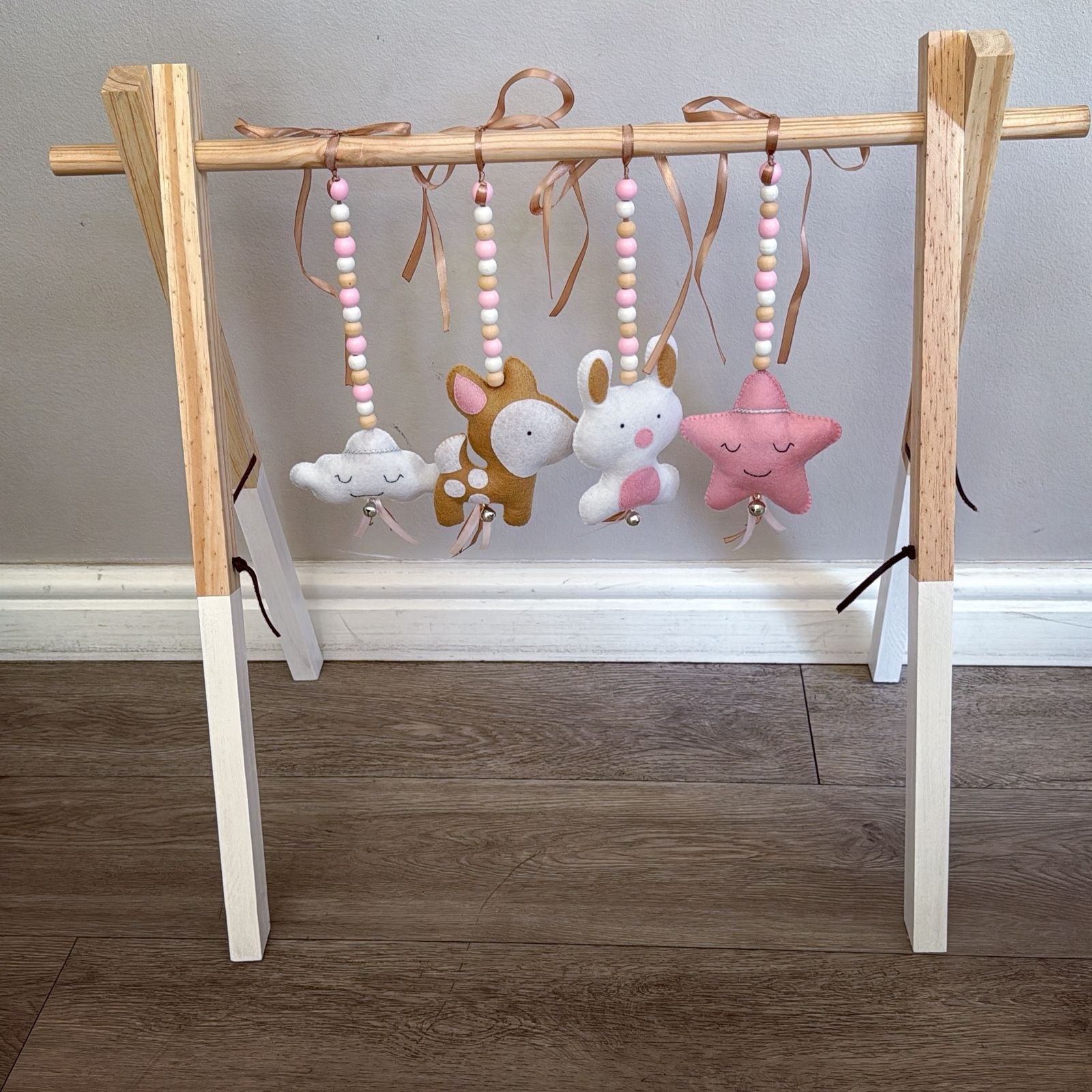 Wooden baby gym with hanging toys on a wooden floor.