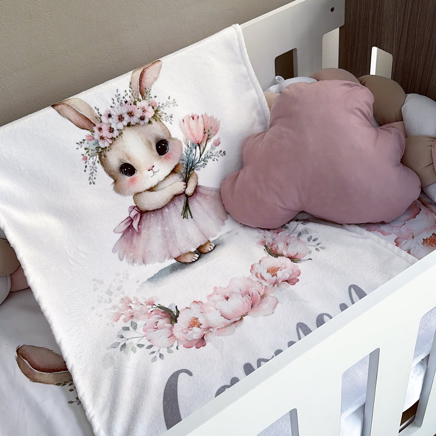 Crib with floral design blanket featuring a cartoon cat in a dress and flower crown.