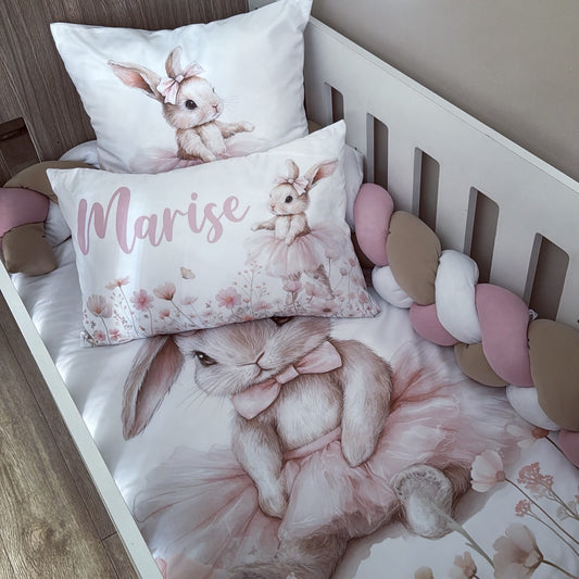 A baby crib bedding set featuring a white and pink bunny print. The set includes a duvet cover with a large sleeping bunny in a pink tutu, a matching pillow with a smaller bunny and the name 'Marise' in pink script, and a white pillow with a bunny illustration.