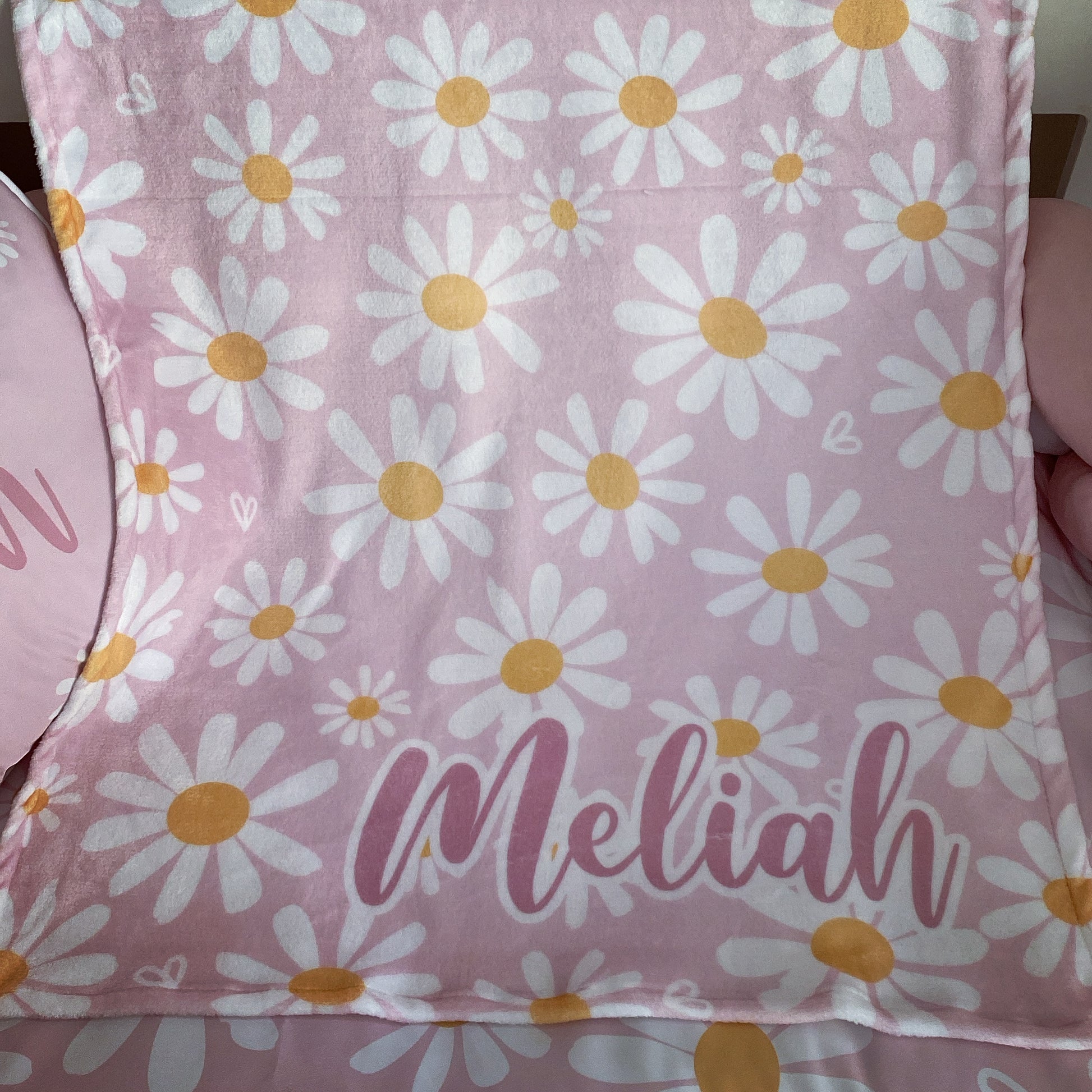 Pink fabric with white daisies and yellow centers, featuring the name 'Meliah'.