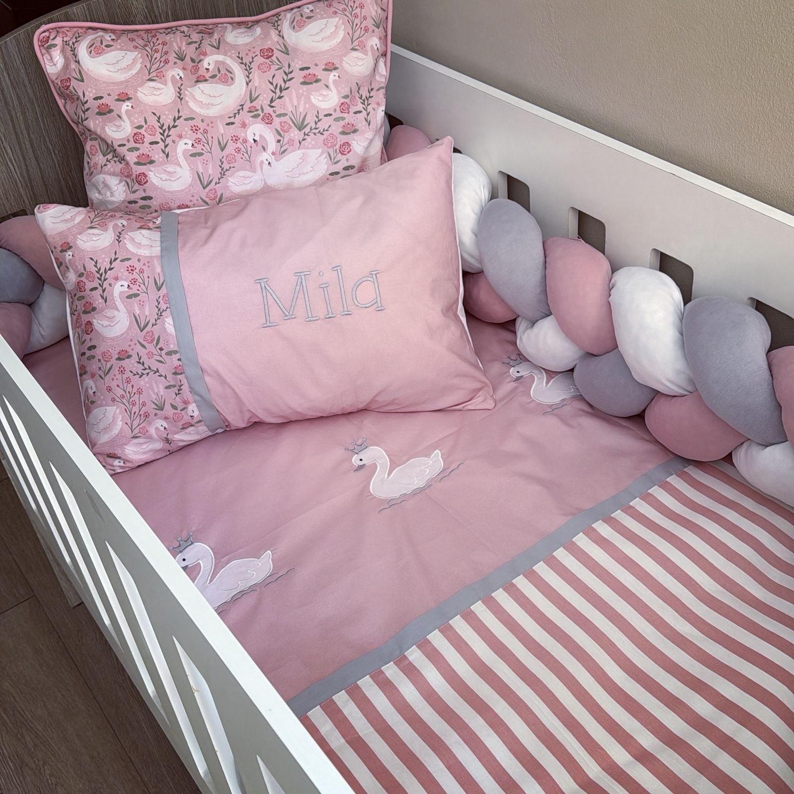 Children's crib with pink bedding and swan design, personalized with 'Mila'.