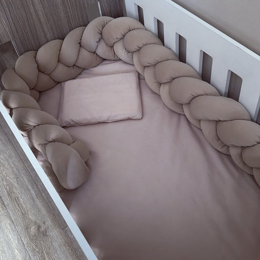 A baby crib bedding set featuring a stone fitted sheet, a matching pillow, and a thick braided bumper pad in a taupe-beige color, shown from an overhead angle.