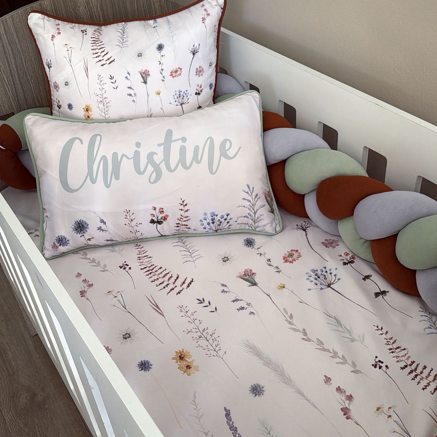 Crib with floral-patterned bedding and pillows, including a pillow with the name 'Christine'.