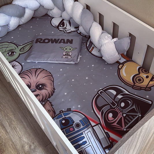 Children's crib with Star Wars-themed bedding featuring characters like Yoda, Chewbacca, R2-D2, and Darth Vader.
