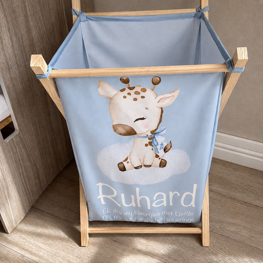 A wooden laundry with a light blue fabric liner featuring a cartoon giraffe and the name 'Ruhard' in white text, shown on a wood floor next to a cabinet.