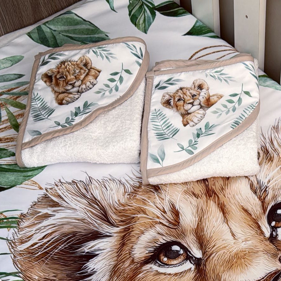 Crib with lion-themed bedding and towels on a wooden floor.