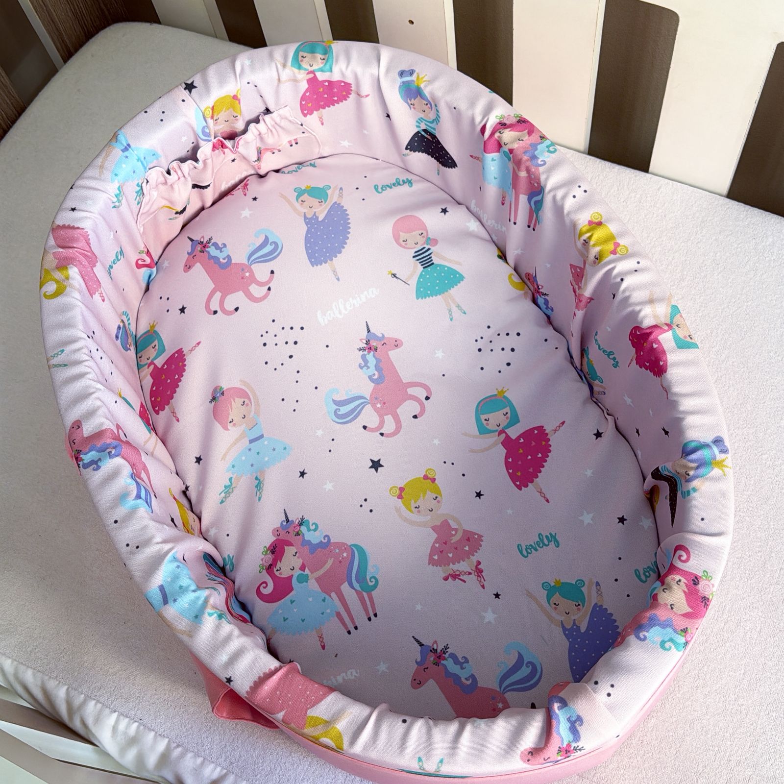 Baby doll carry cot with fairy and unicorn pattern on a white surface