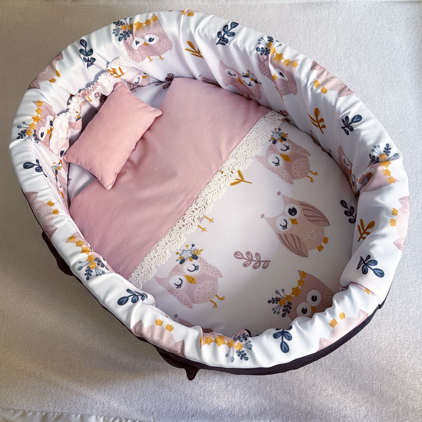Baby crib with pink bedding and owl patterned sides on a light background