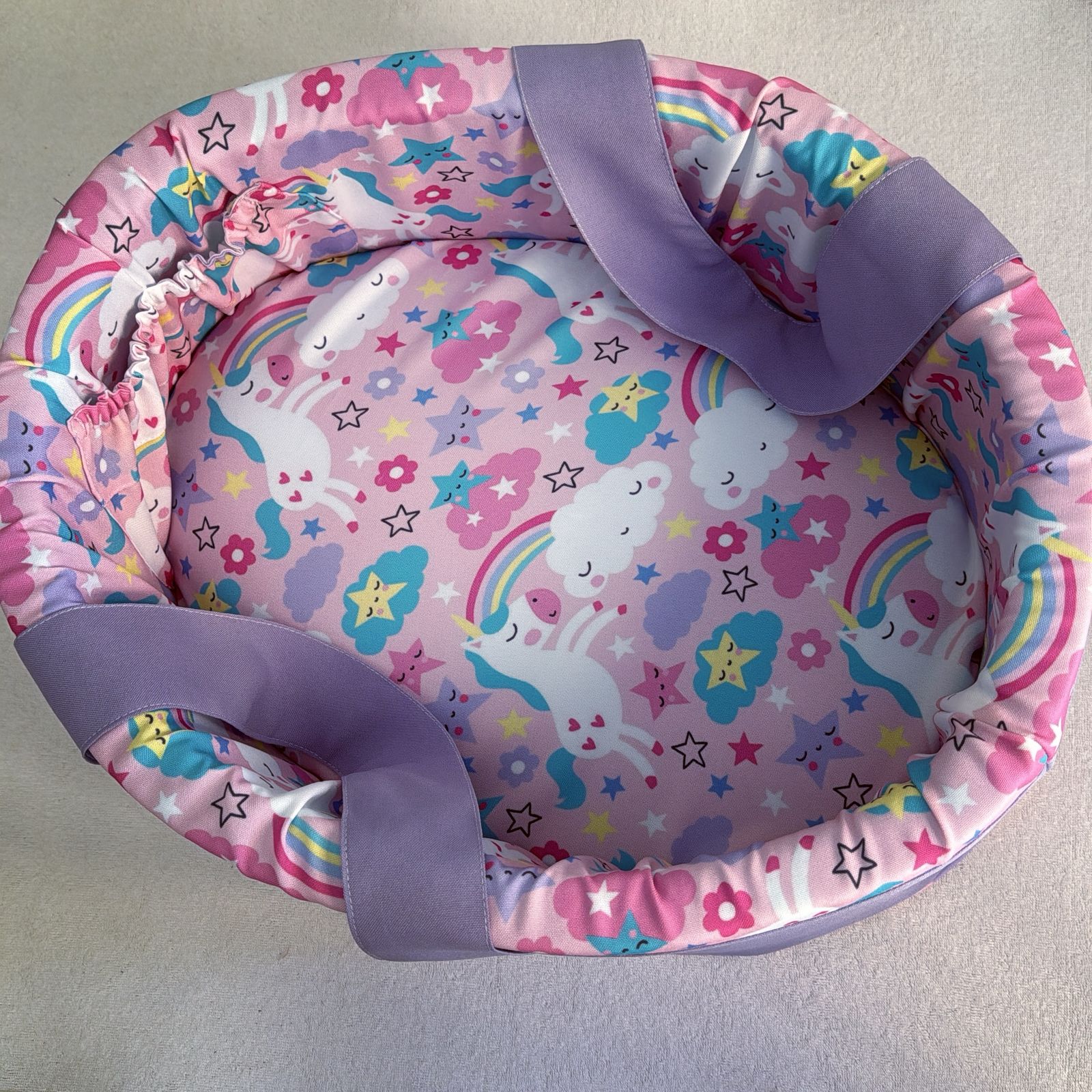 Pink baby seat with unicorn and rainbow pattern on a light gray background