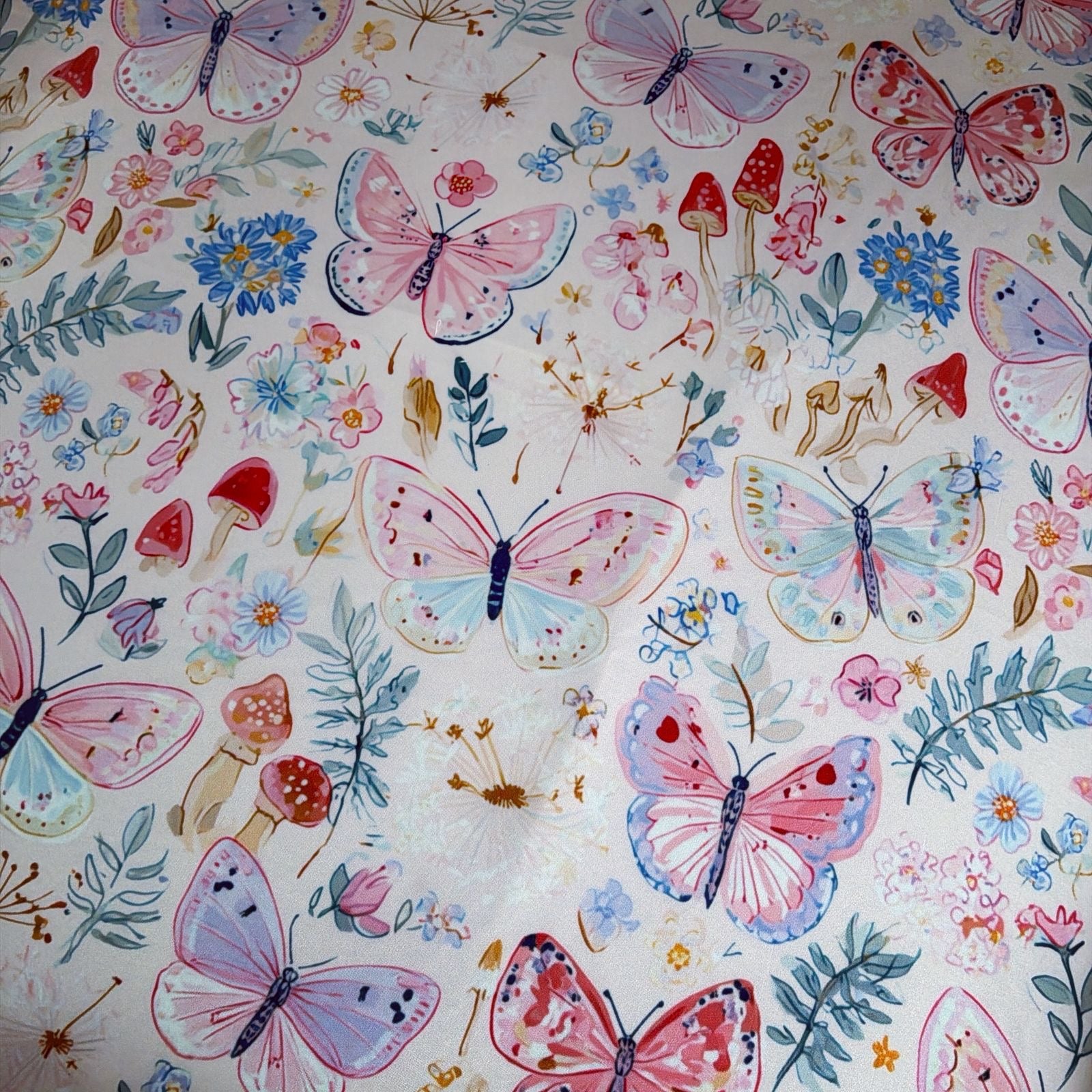 A close-up of a baby doughnut mat featuring watercolour-style butterflies, flowers, leaves, and small mushrooms on a light cream background.