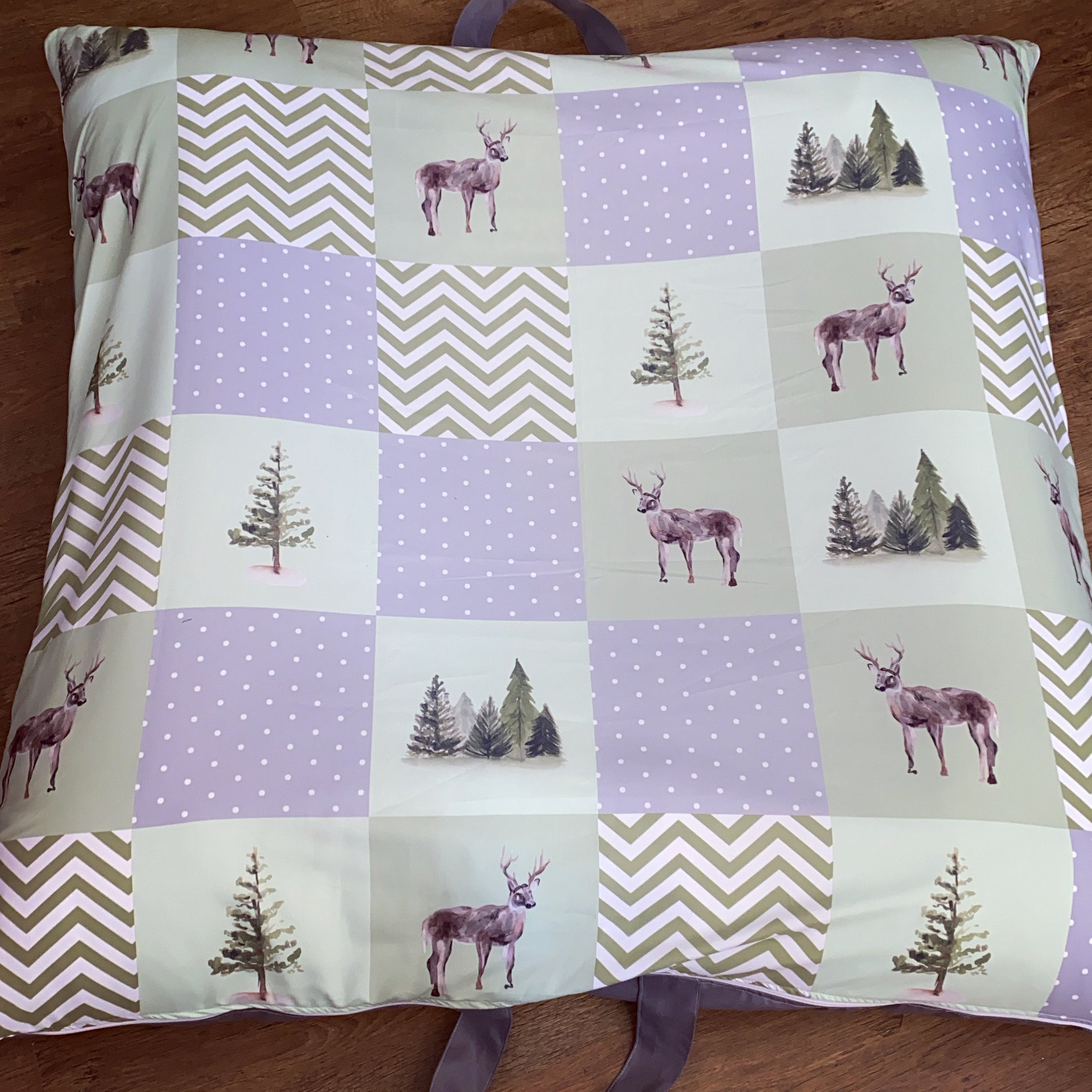 Patchwork pillow with deer and tree patterns on a wooden surface