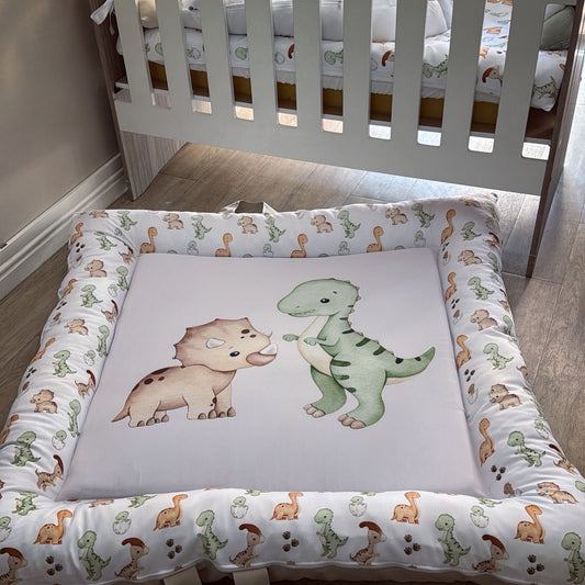 Baby crib with dinosaur-themed bedding and mattress pad in a nursery setting.
