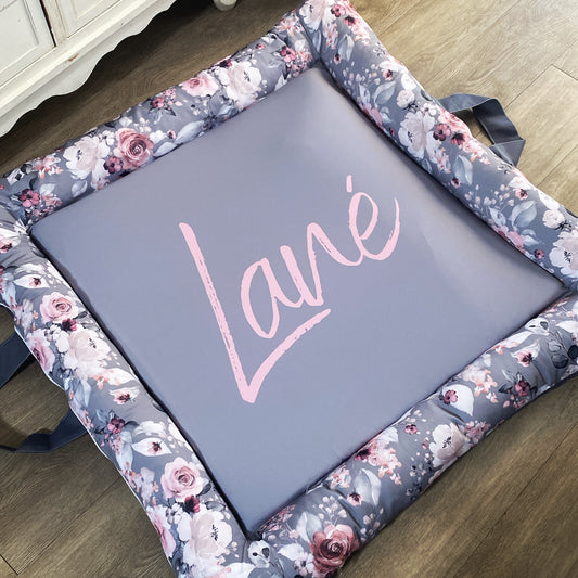 A gray baby play doughnut with a floral pattern around the edge and the name 'Lana' written in the center.