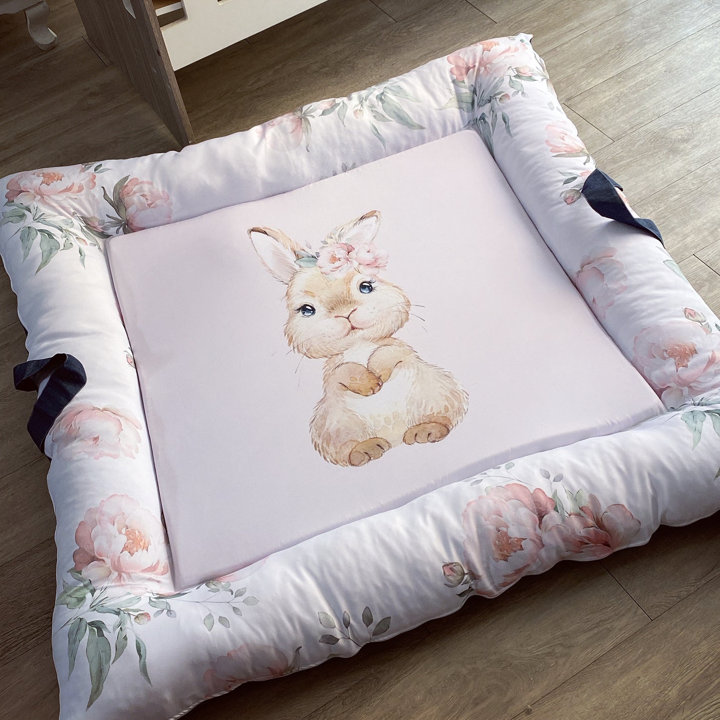A floral-patterned baby play doughnut with a central illustration of a bunny, with washable cover and side handles.