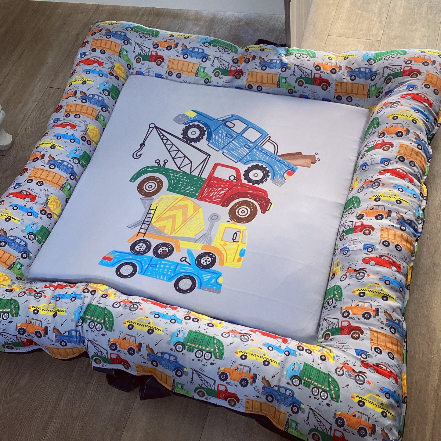 A colorful baby play doughnut with a transportation theme, featuring various vehicles such as cars, trucks, and trains in a patterned design.