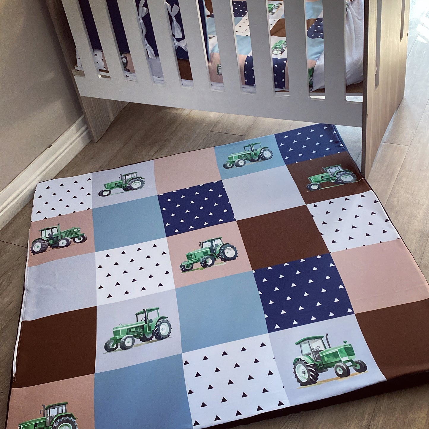 A multicolored foam playmat featuring a farm animal theme with tractors and crops, placed in a nursery room near a wooden crib.