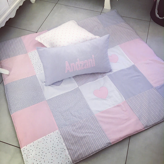 Patchwork blanket with pink and gray squares and a heart design, featuring a pillow with 'Andzani' on a tiled floor.