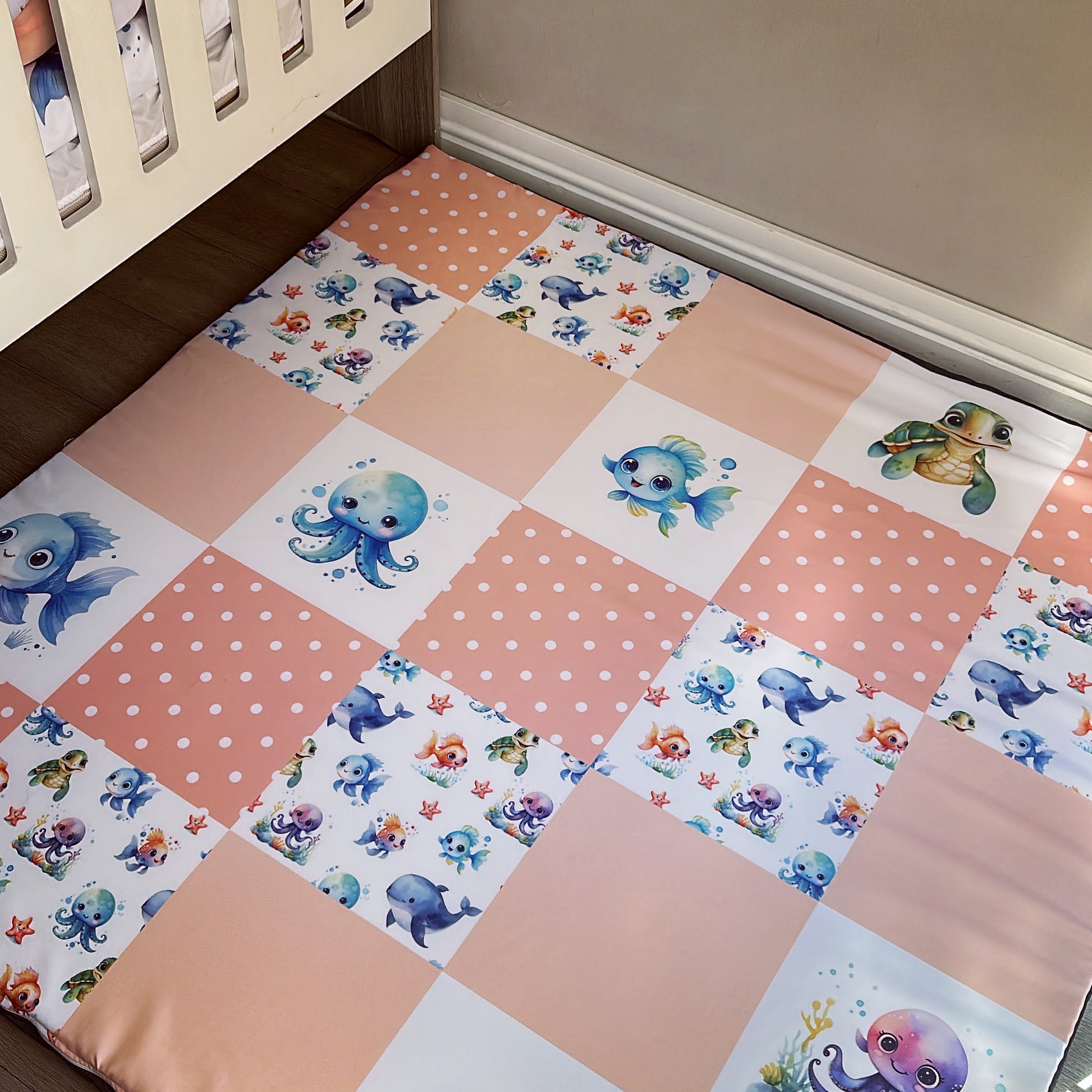 A large pink playmat with an ocean theme, featuring various sea creature illustrations, placed on the floor next to a baby's crib.