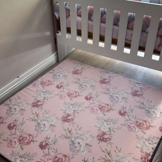 Floral mattress cover on a crib with a pink and gray patterned blanket.
