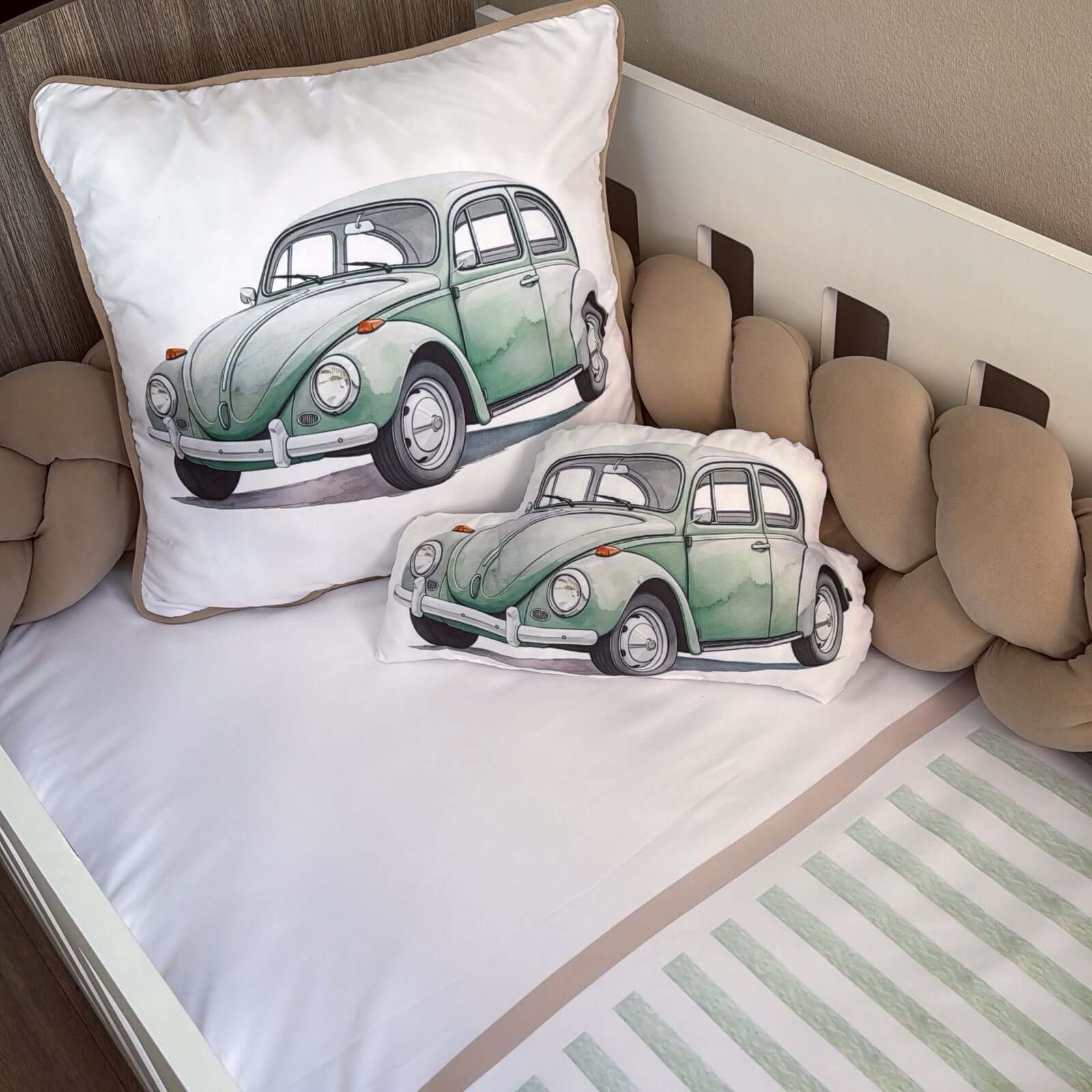 Two pillows with green car designs on a crib with beige bedding.