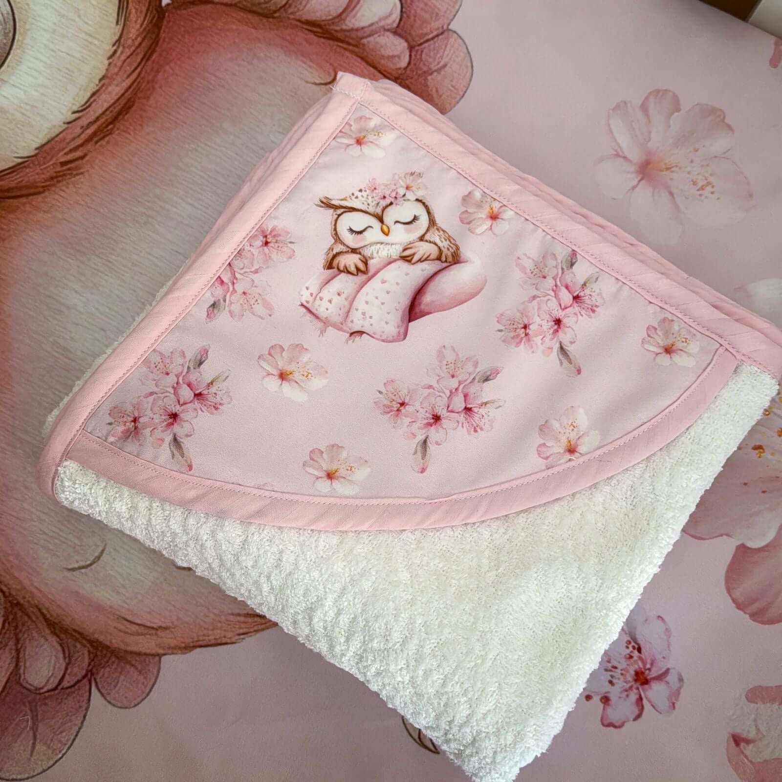 Baby hooded towl with owl design held by a hand on a floral background