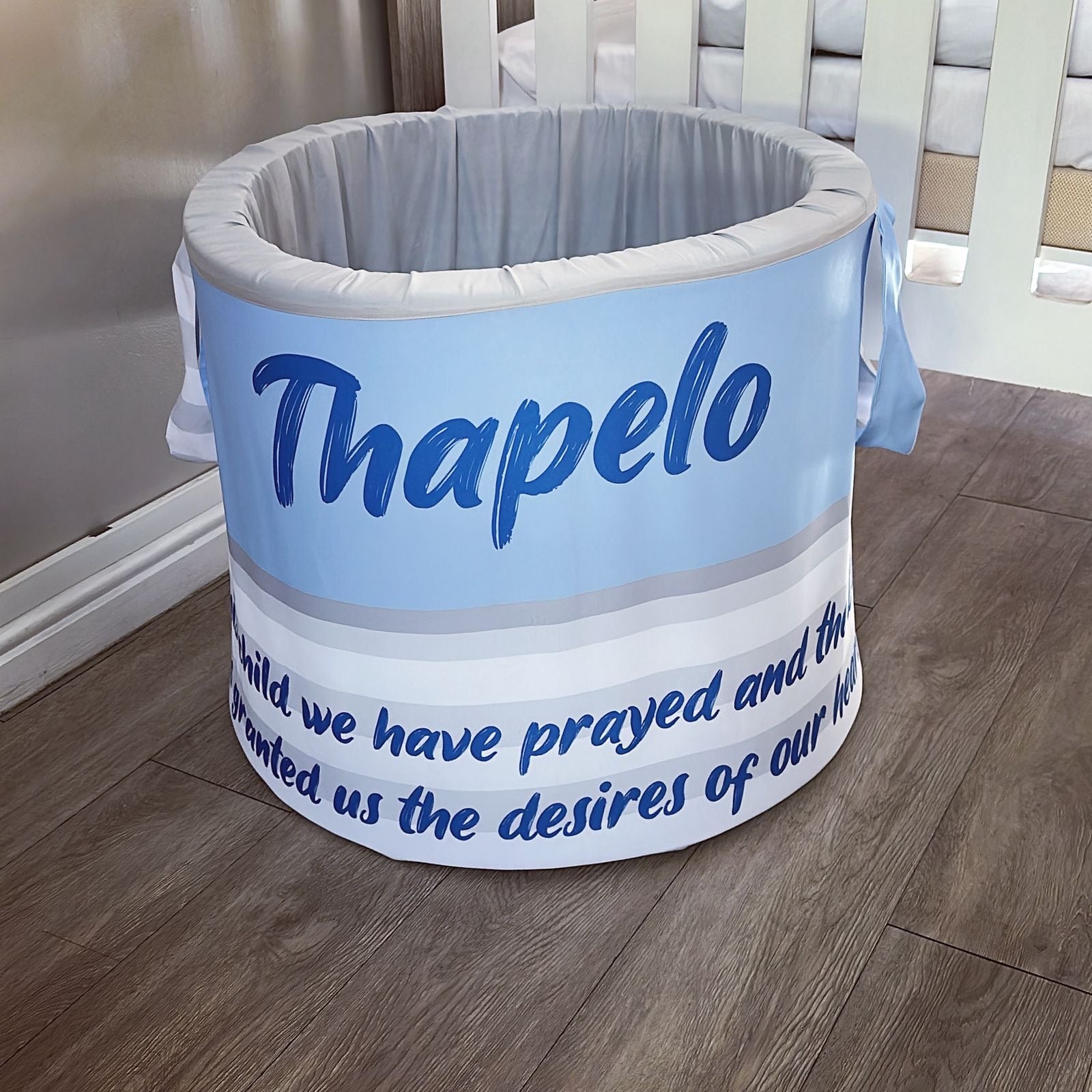 Round baby laundry barrel with 'Thapelo' branding on a wooden floor.