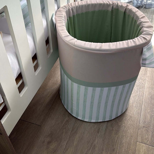Green and white striped laundry basket on a wooden floor next to a crib