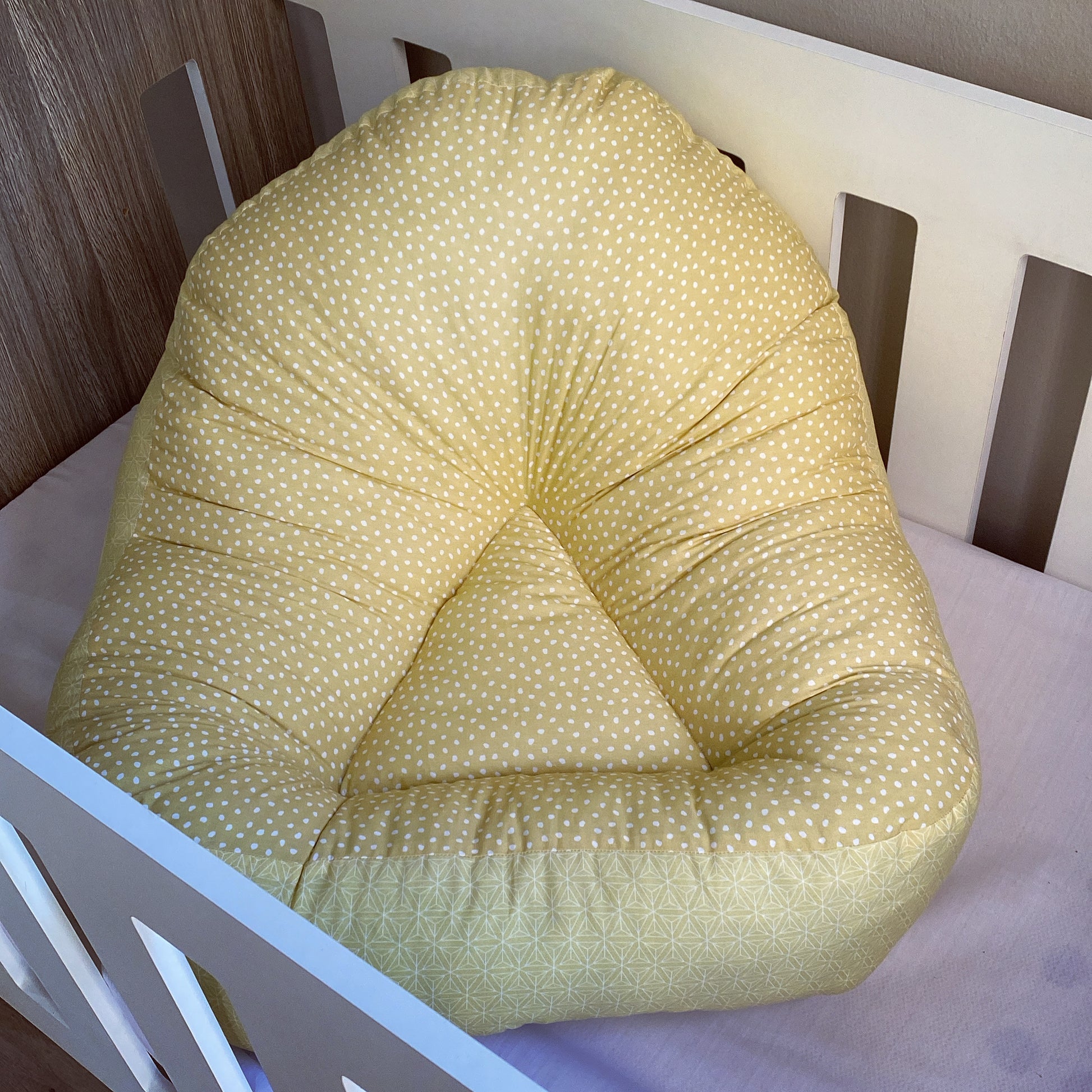 A yellow lounger with mustard dots pattern placed in a white crib.