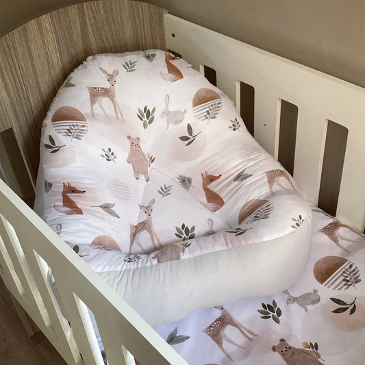 A white fabric lounger with a woodland animal print, positioned in a wooden crib.