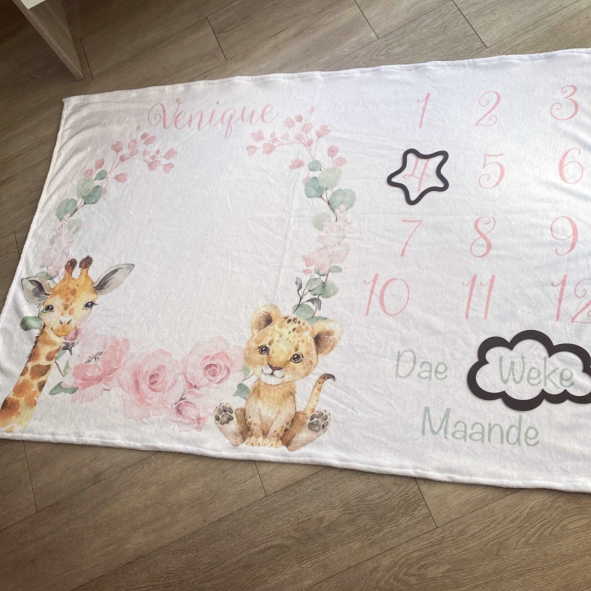 Baby milestone blanket with lion and giraffe illustrations and numbers on a wooden floor.