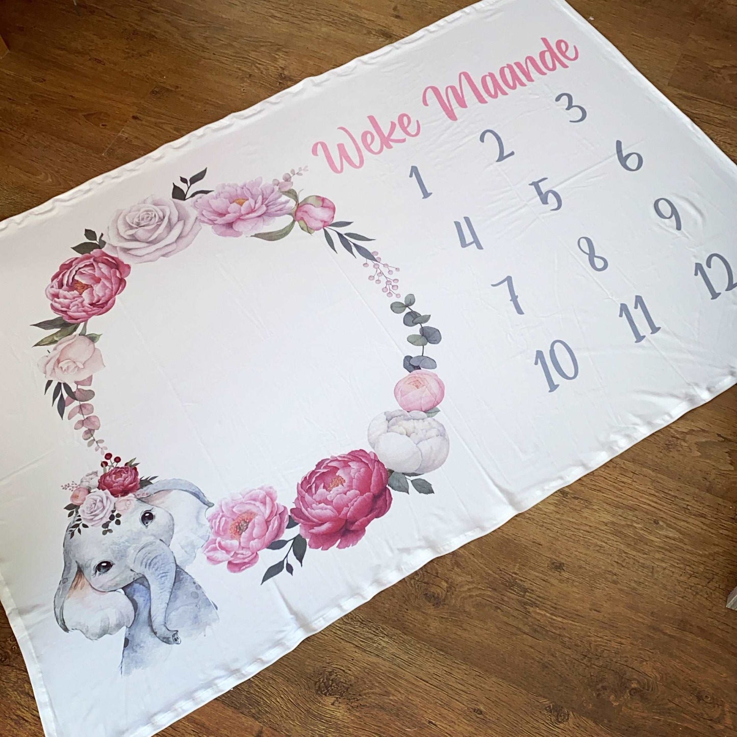 Baby milestone blanket with elephant and floral design on a wooden surface