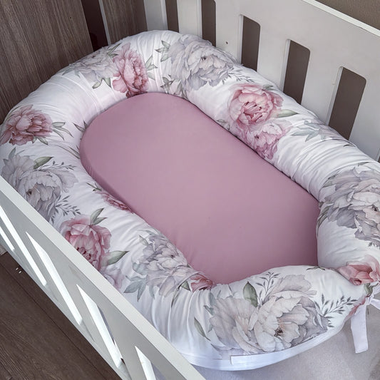 Floral-patterned baby nest with pink interior on a wooden floor.