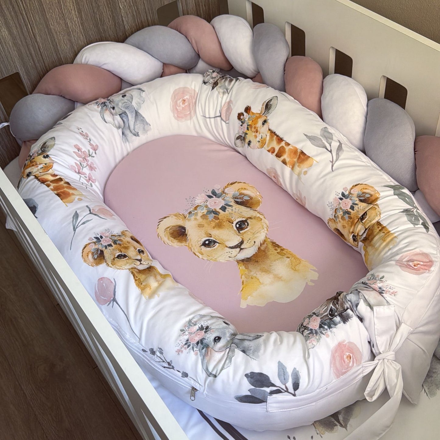 Baby crib with a lion-themed bumper and pink mattress