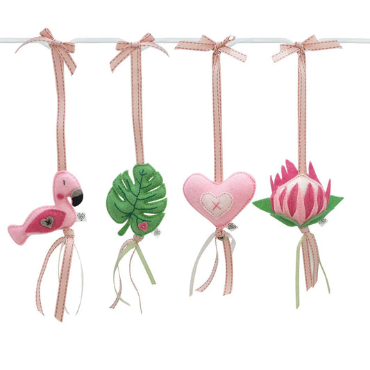 Four pink and green felt hanging ornaments shaped like a flamingo, a monstera leaf, a heart, and a protea flower, suspended from a white rod with pink ribbons on a white background.