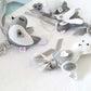 A set of handmade felt animal ornaments, including a seal, a rabbit, and a sheep, crafted from gray and white felt with silver-gray ribbons, displayed on a white textured fabric background. | Baby Essentials | All Baby Products | Soft Spot Kids | South Africa