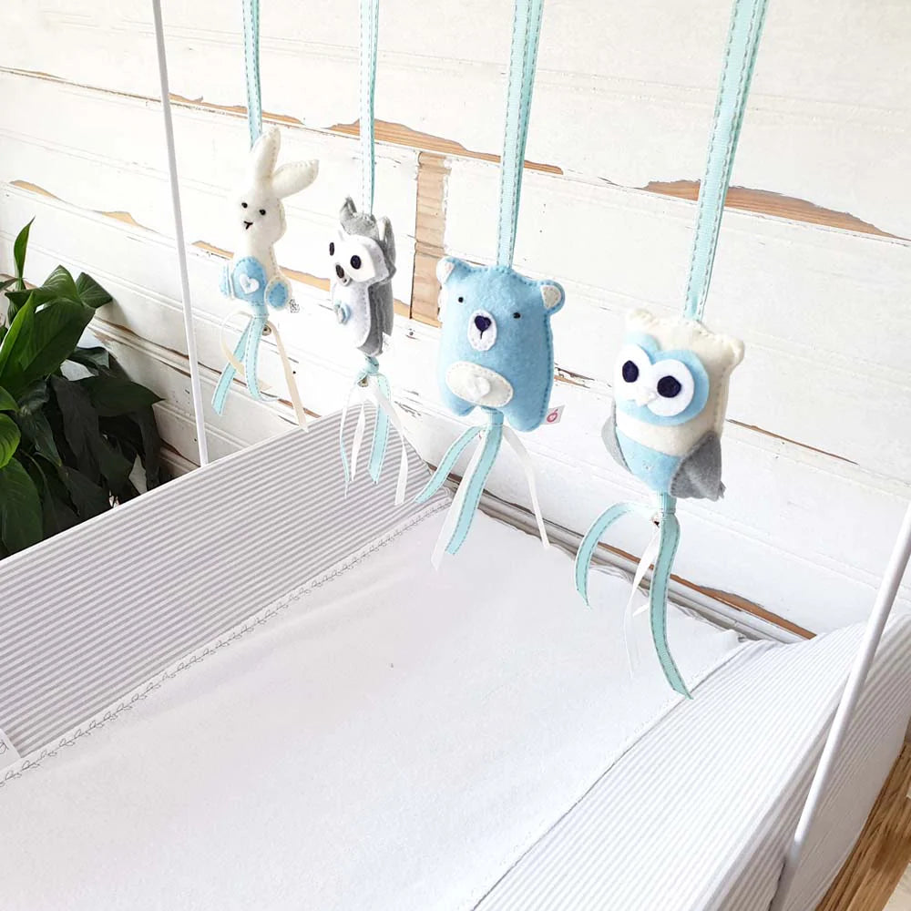 A soft baby crib hanging toy set with four plush animal figures suspended by mint blue ribbons. The figures include a white rabbit, a gray wolf, a light blue bear, and a blue-and-white owl, arranged on a white crib against a white rustic wood wall.