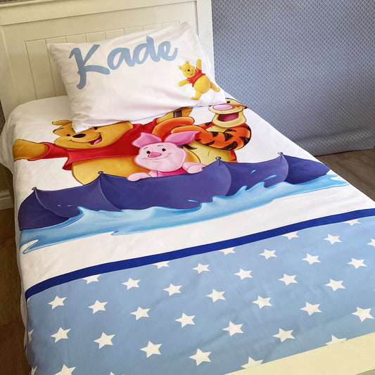 A toddler bedding set with Winnie the Pooh characters in blue, featuring a boat design and stars on a white background.