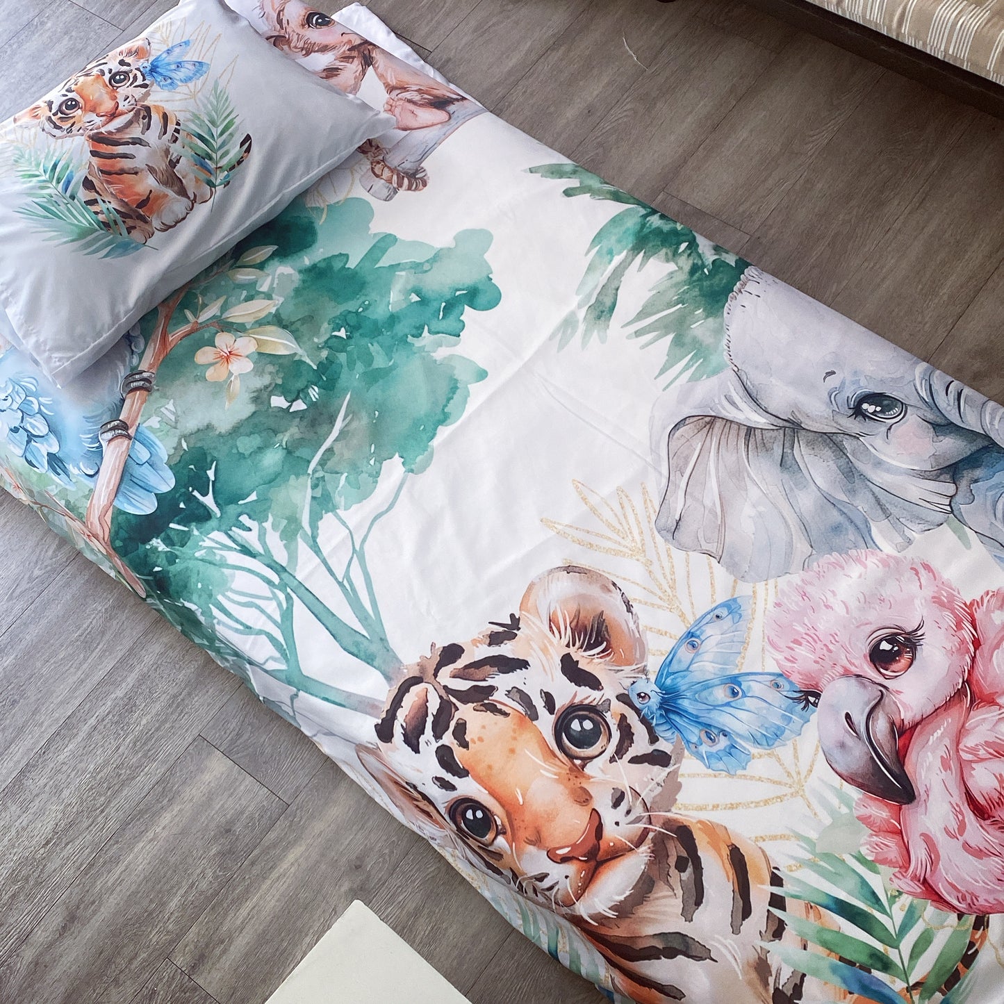 A toddler bedding set with a jungle theme, featuring illustrations of a tiger, elephant, and other jungle animals, along with leaves and flowers in a colorful palette.