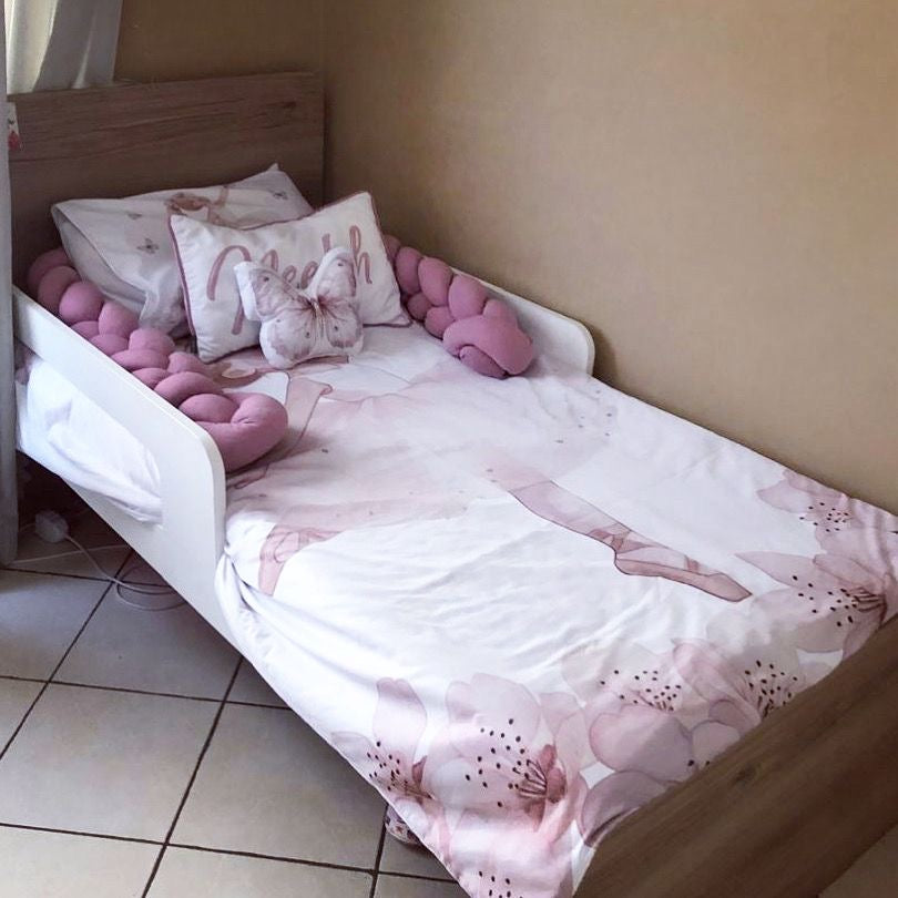Children's bed with pink floral bedding and decorative pillows in a room.