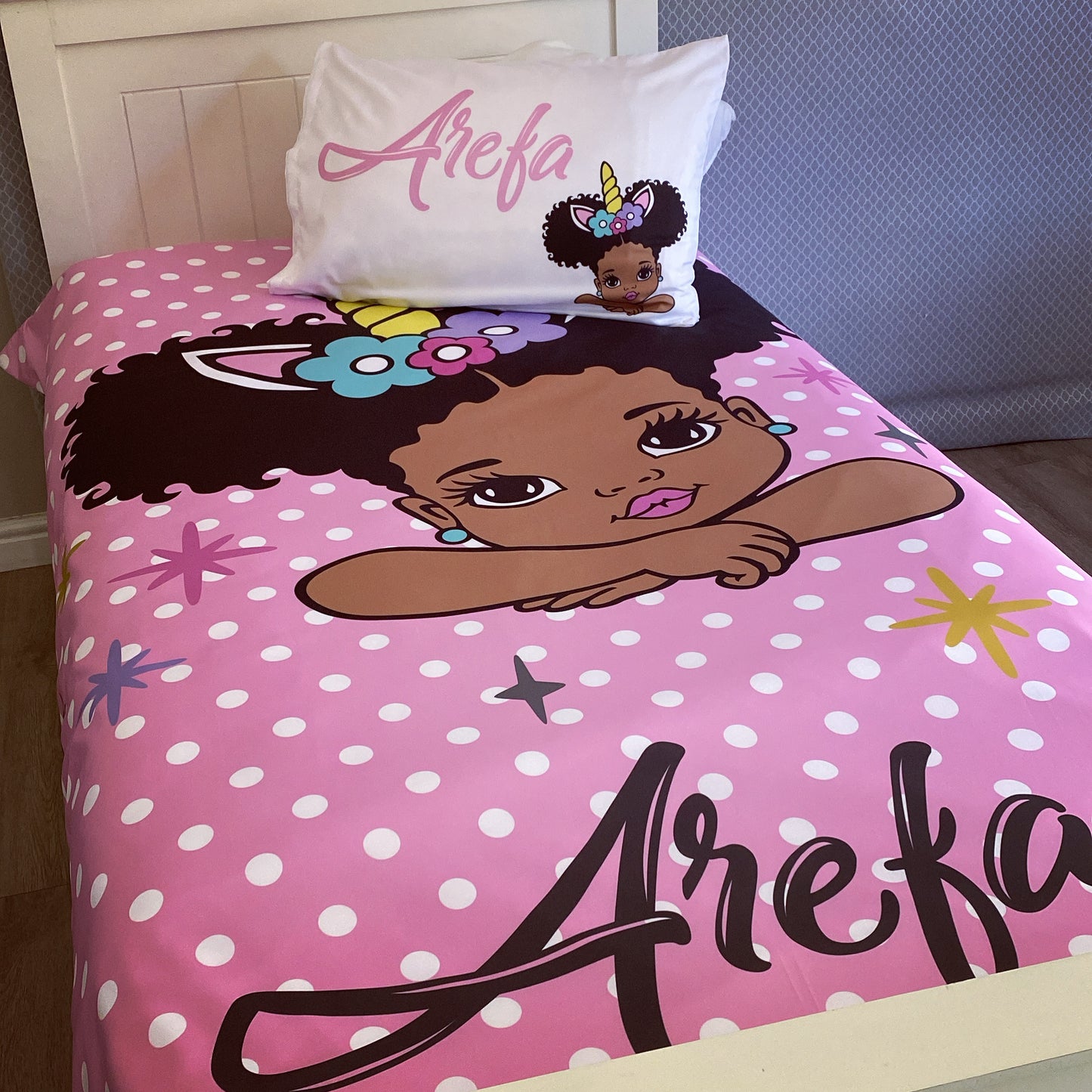 A toddler bedding set with a pink background featuring a character illustration and polka dots. The set includes a pillowcase with a character design and the name 'Arefa' printed on it.