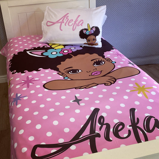 A toddler bedding set with a pink background featuring a character illustration and polka dots. The set includes a pillowcase with a character design and the name 'Arefa' printed on it.