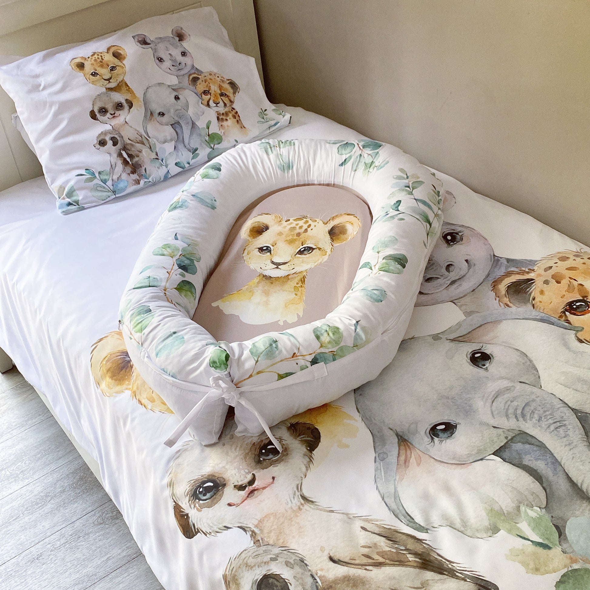 A toddler bedding set with a safari animals theme, including a duvet cover and pillowcase with illustrations of a lion, elephant, and other animals.