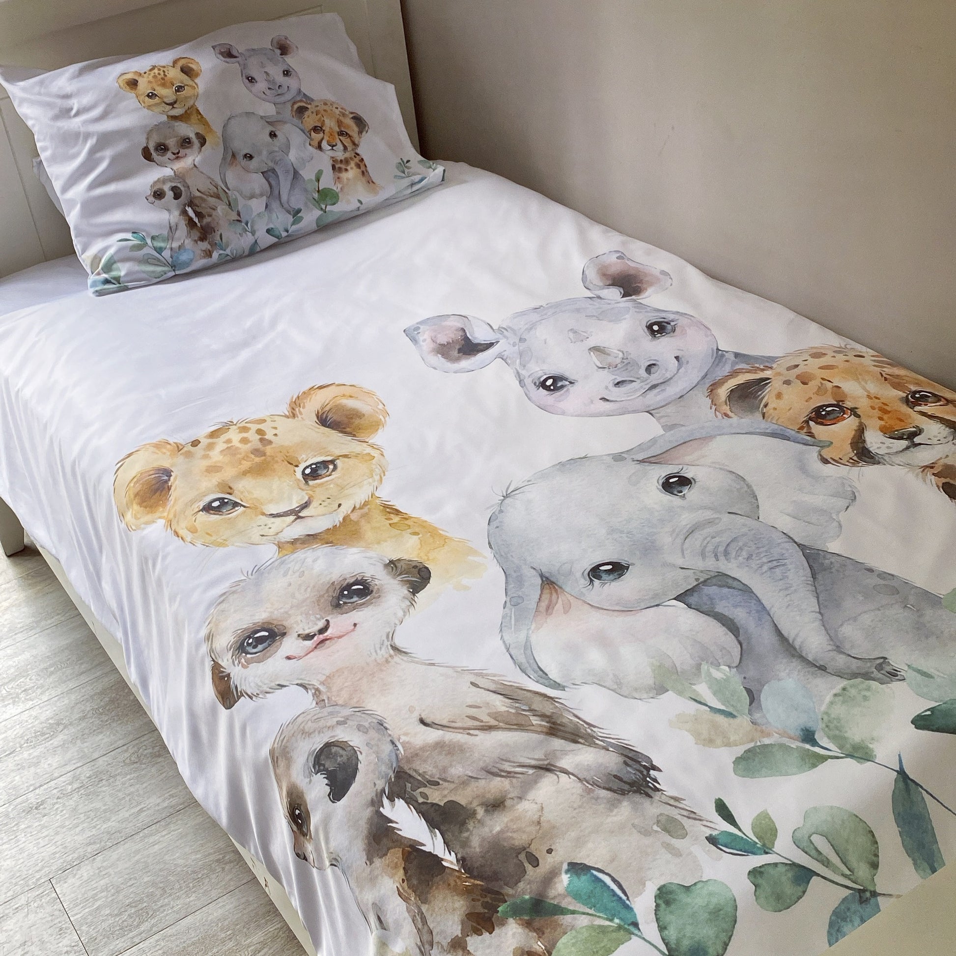 A toddler bedding set with a safari animals theme, including a duvet cover and pillowcase with illustrations of a lion, elephant, and other animals.
