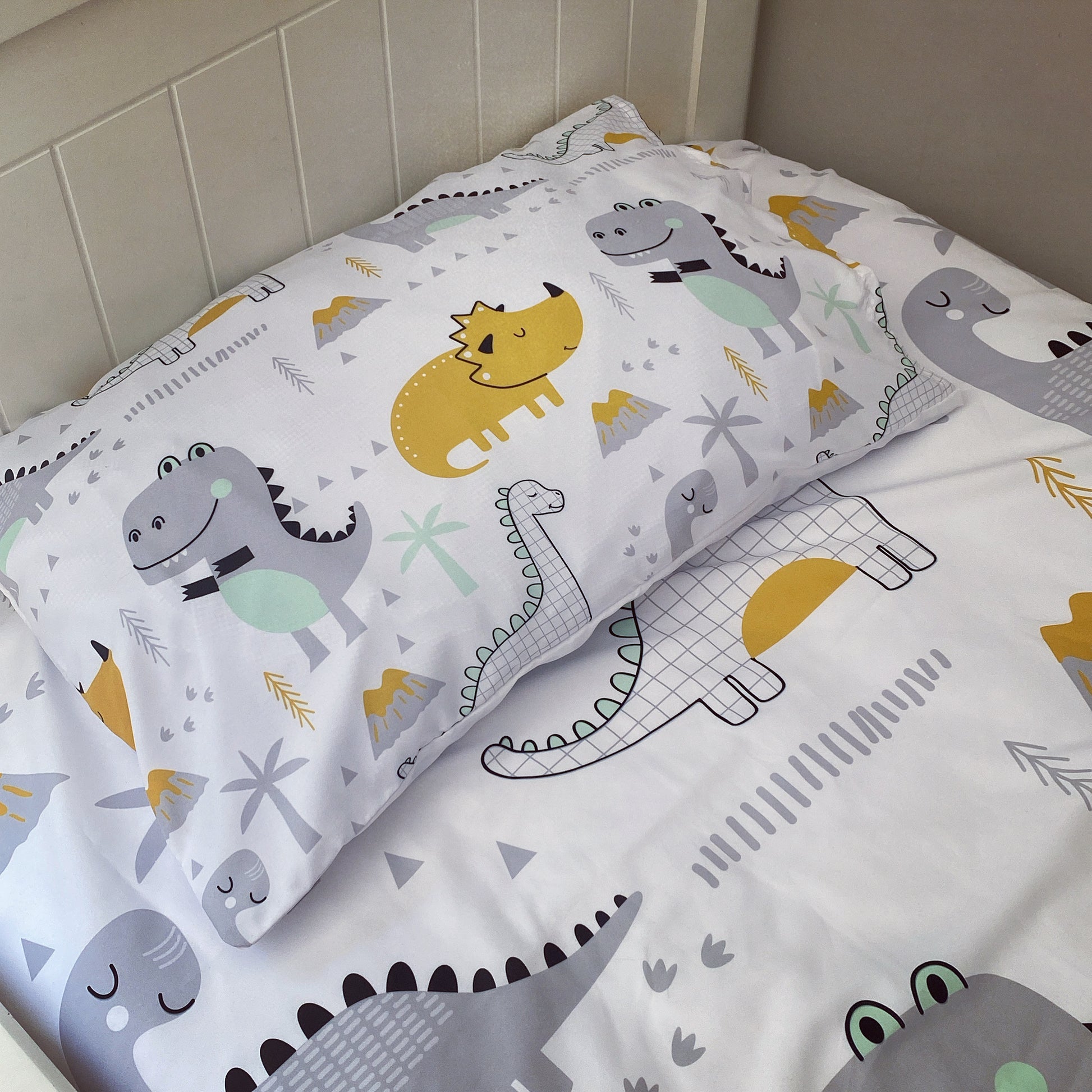 Children's dinosaur-themed pillowcase and sheet set on a bed.