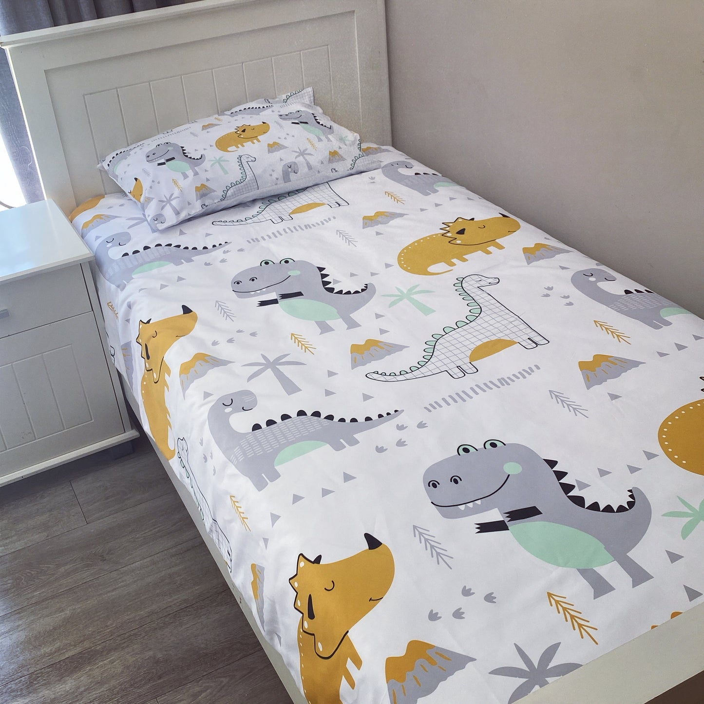 Children's dinosaur-themed bed sheet set on a bed in a room.