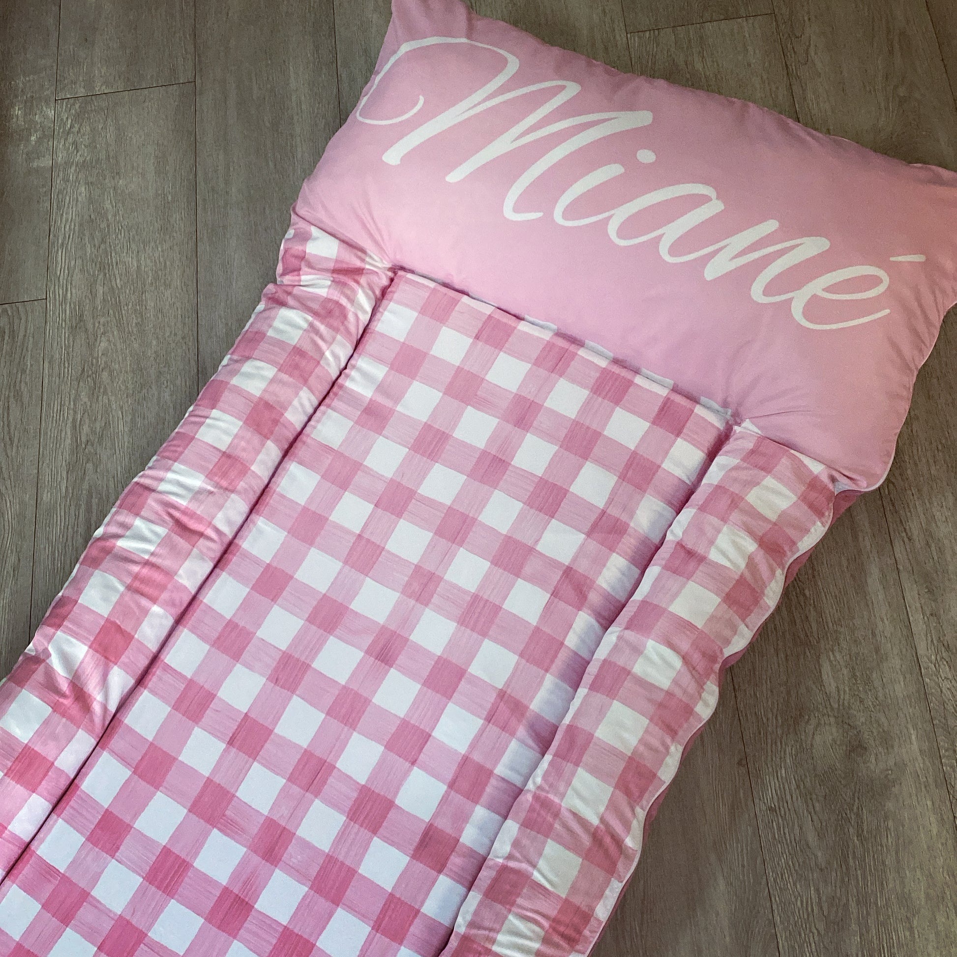 Pink checkered blanket with 'Miane' printed on a wooden floor